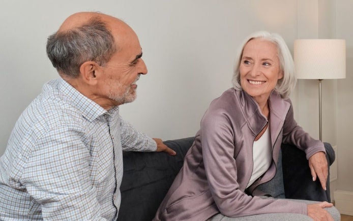 Un hombre y una mujer de edad avanzada, sentados en un sofá, se sonríen mutuamente, conscientes de que cuentan con el respaldo de la gama de productos para alimentación por sonda de Fresubin, que incluye Frebini ORIGINAL FIBRE, Fresubin ENERGY y Supportan Tube Feeds. 