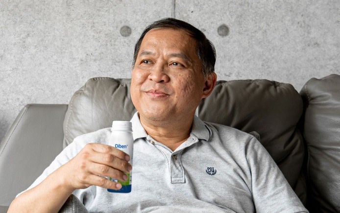 A man sits on a sofa and smiles as he enjoys a Diben Drink, part of Fresubin's Diben range designed to support the nutritional needs of those with diabetes. 