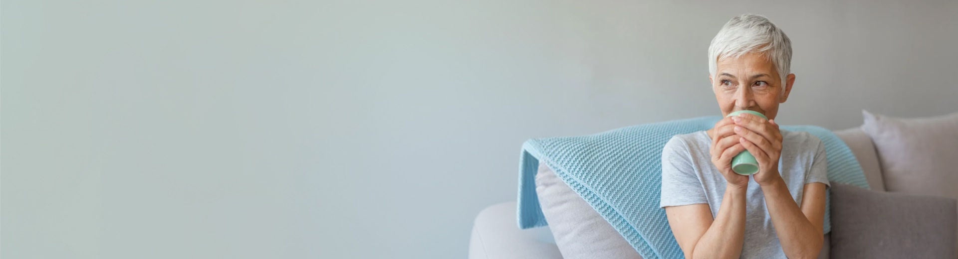 Persoon zit in een zetel in een huiselijke omgeving en houdt een mok in de handen.