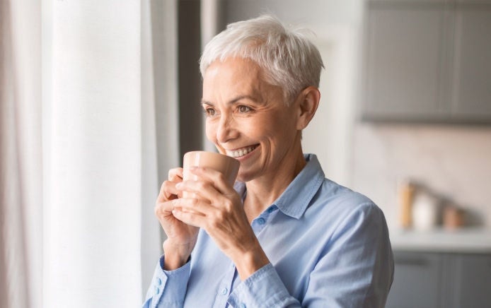 Een vrouw met een blauwe hoofddoek en blouse praat met een vriendin terwijl ze geniet van Fresubin’s Supportan-drank met cappuccinosmaak, bedoeld om te voorzien in de voedingsbehoeften tijdens kanker en de behandeling 