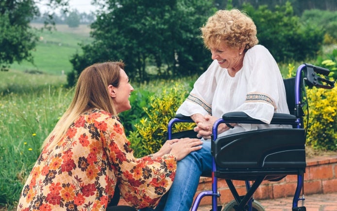 Una mujer en silla de ruedas le sonríe a una mujer más joven que está agachada frente a ella, consciente de que cuenta con el respaldo de la gama de productos Fresubin para complementar su ingesta nutricional. 