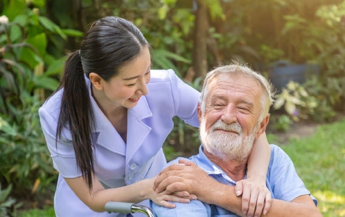 An elderly man sits in a wheelchair as he smiles with the lady behind him knowing he is supported by Fresubin's PRO range, designed to improve the protein intake of older adults. 