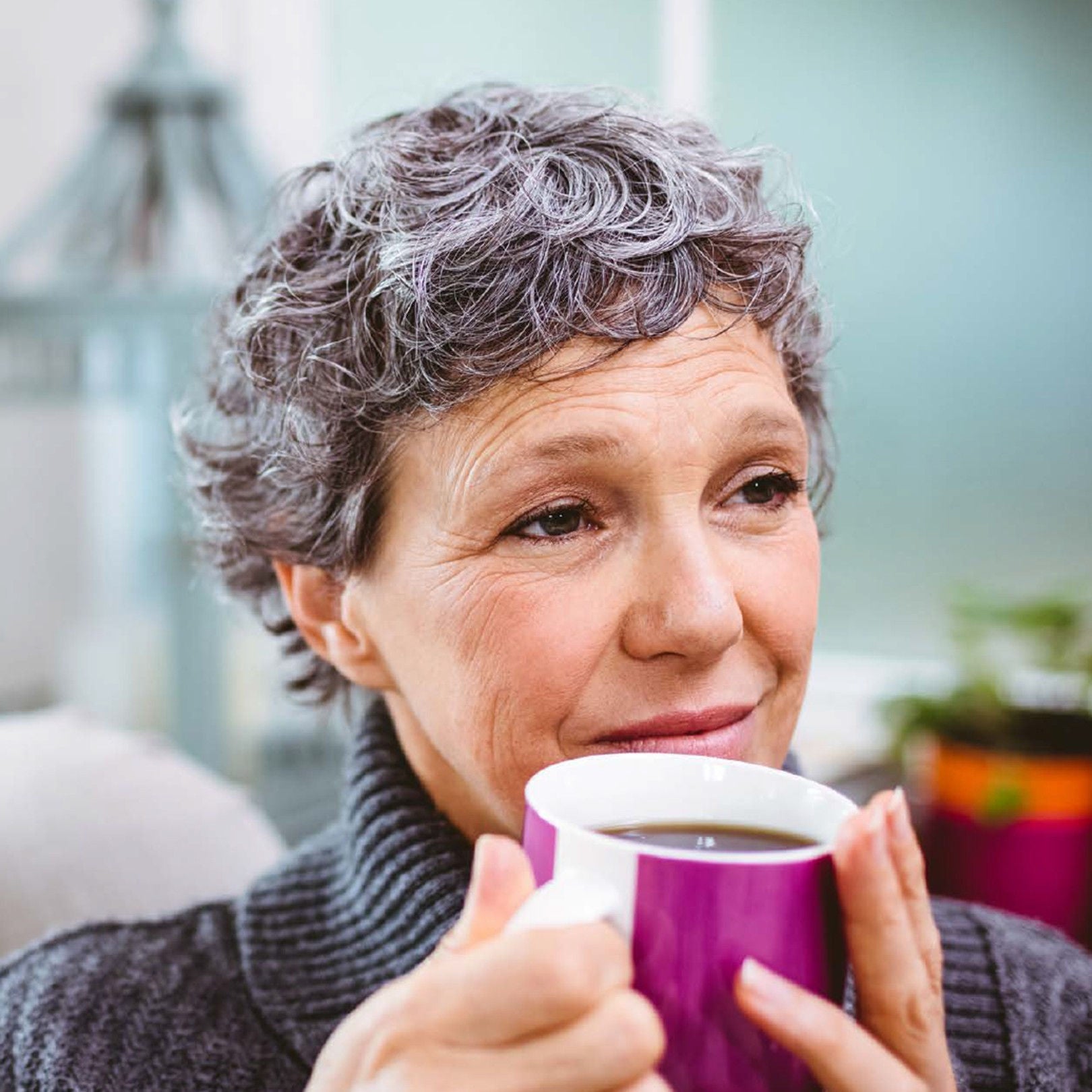A woman with short curly grey hair smiles gently while holding a purple mug of coffee knowing she is supported by Fresubin’s range of nutritional supplements 