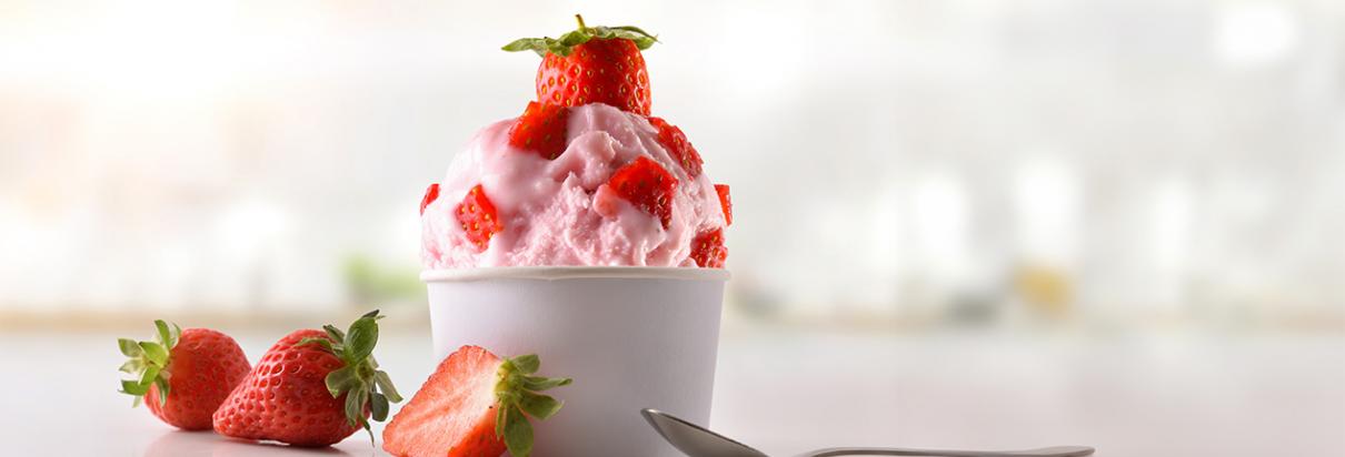 Eine Kugel Erdbeereis im Becher mit Erdbeeren dekoriert