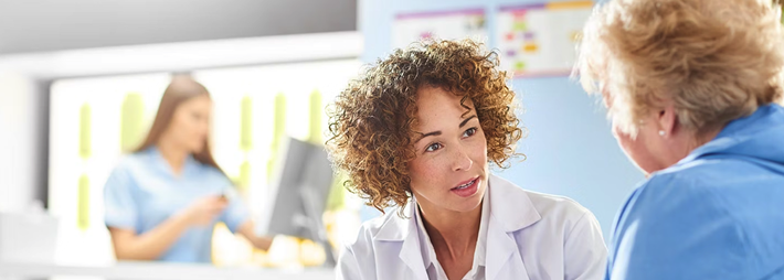 Female healthcare professional speaking with an older patient during a medical consultation in a clinical setting.