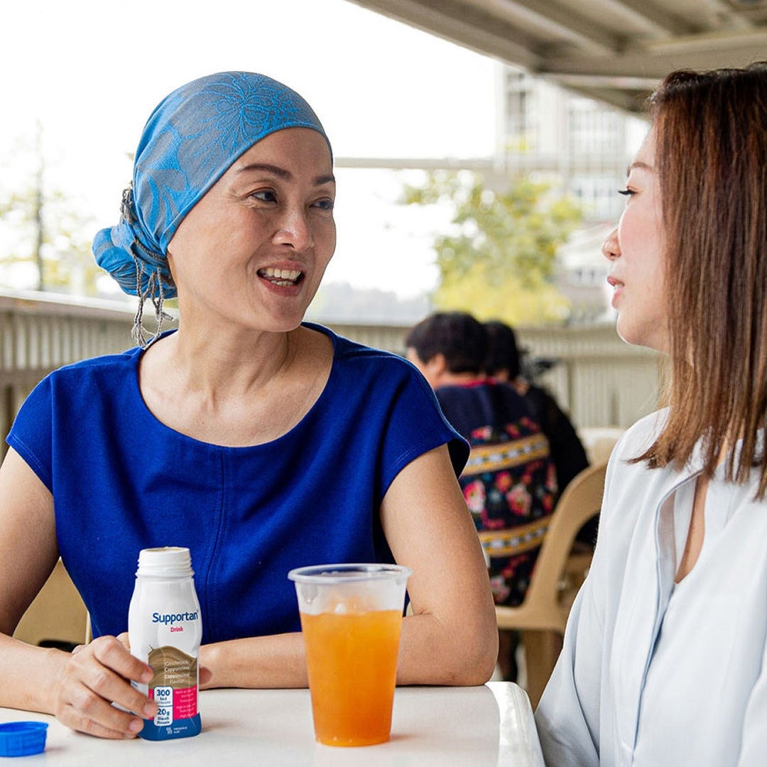 A woman with short curly grey hair smiles gently while holding a purple mug of coffee knowing she is supported by Fresubin’s range of nutritional supplements 
