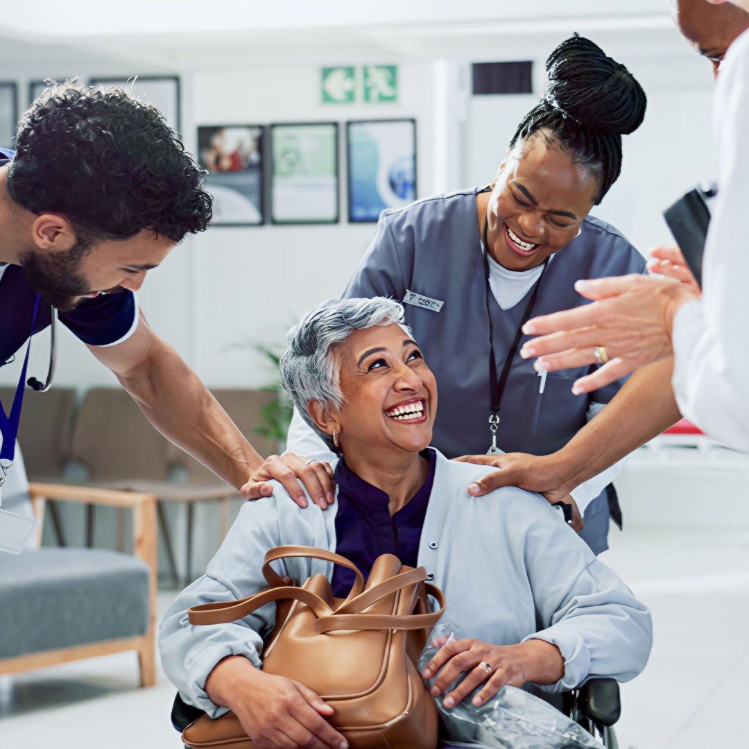 Maria sits in a wheelchair as she smiles up towards her healthcare professionals who helped her regain her weight and energy with Fresubin nutritional supplements during her colorectal cancer treatment. 