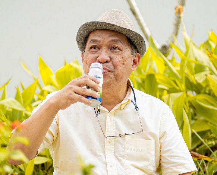 Un hombre, en su jardín, disfruta de una bebida Diben con sabor a vainilla para satisfacer sus necesidades nutricionales como persona con diabetes. 