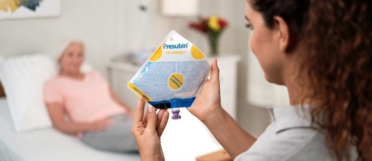 Sveikatos priežiūros specialistė laikanti enterinės mitybos mišinio maišą