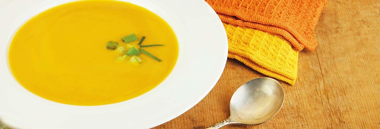 Ein Teller Curry mit Lauch Garnierung steht auf einer Holzoberfläche. Daneben ein Löffel und zwei gelb- und orangefarbige Stoffservietten..