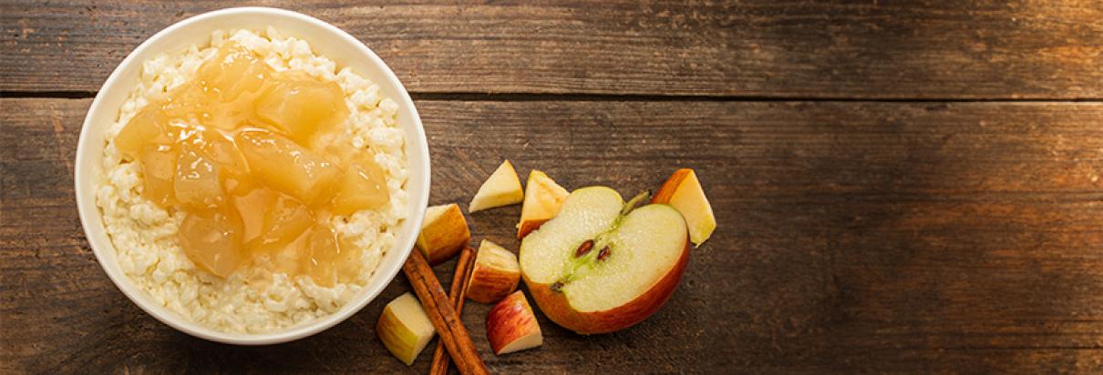 Veganer Apfel-Zimt-Milchreis mit Apfelkompott in einer Schale und aufgeschnittenen Apfelstücken nebendran  