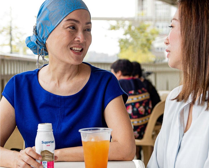 A woman with short curly grey hair smiles gently while holding a purple mug of coffee knowing she is supported by Fresubin’s range of nutritional supplements 
