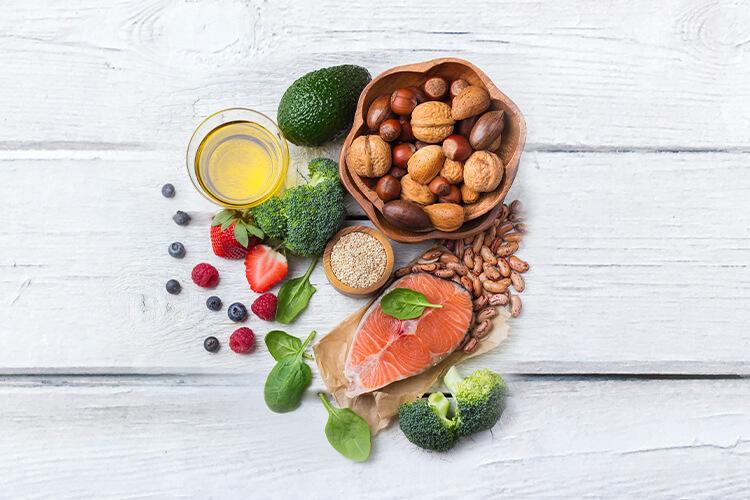 Gesunde Lebensmittel wie Nüsse, Lachs, Avocado, Brokkoli und Beeren auf Holztisch.