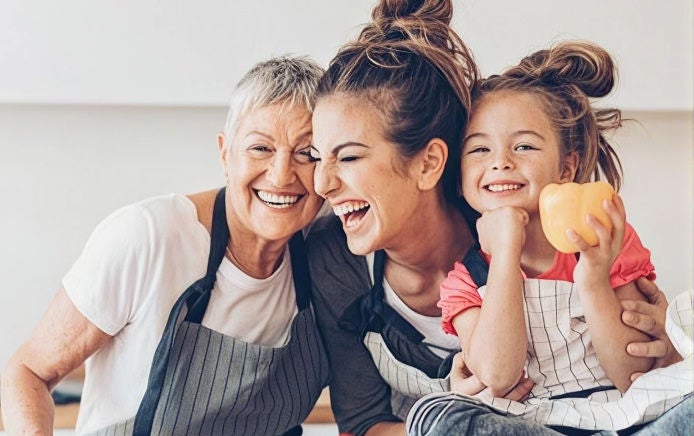 Drie personen staan samen al lachend in een keukenomgeving. Eén persoon houdt paprika vast.