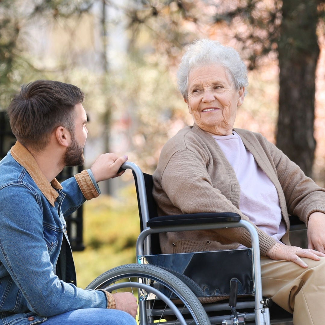 An older lady in a wheelchair smiles towards the younger man crouching next to her knowing she is supported by Fresubin's nutritional support range. 