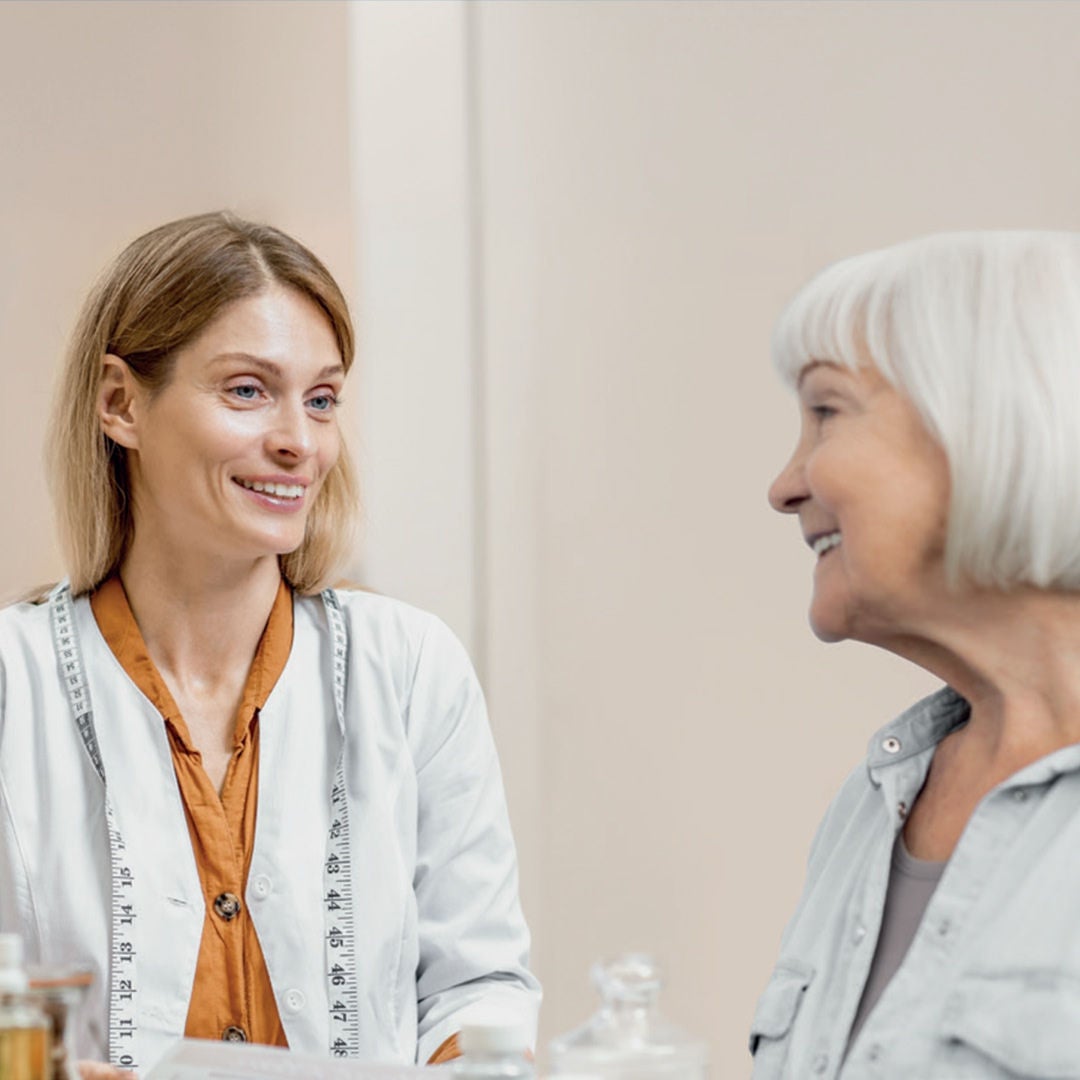 An older lady smiles with her healthcare practitioner as they discuss the right Fresubin oral nutritional supplements to suit her needs. 