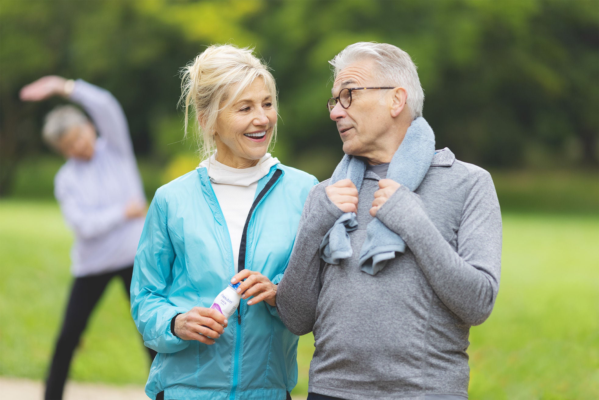 Patientin und Ehemann sind im Park Sport machen. In der Hand hält sie eine Fresubin Flasche.