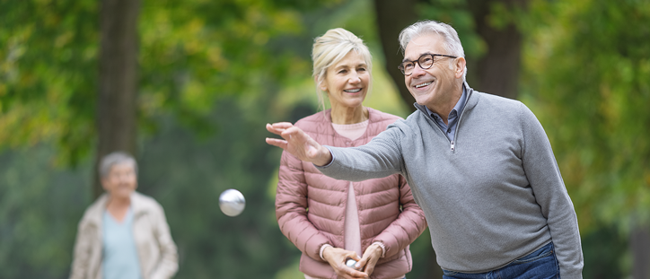 Seniorenpaar spielt lachend Boule im Park.