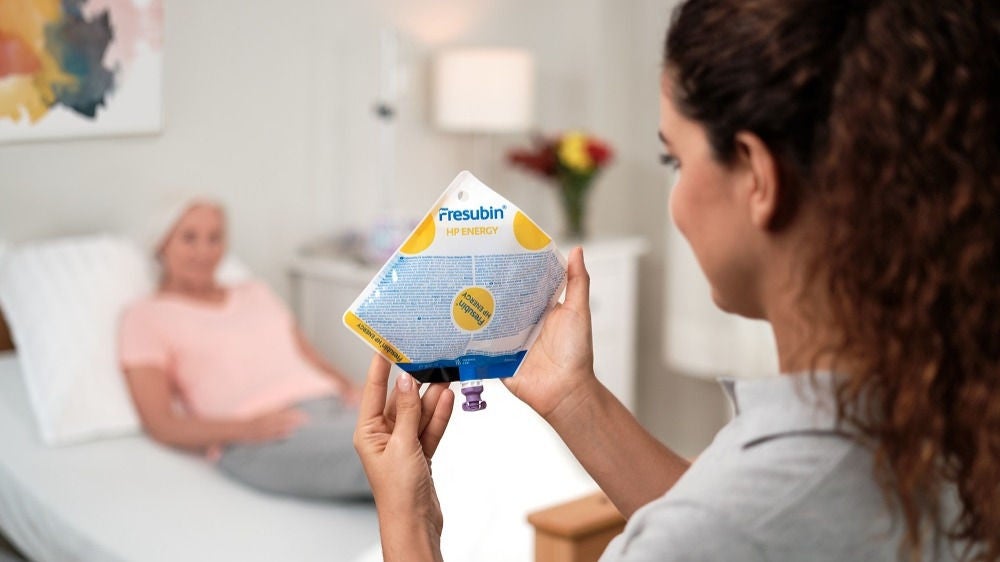 Sveikatos priežiūros specialistė laikanti enterinės mitybos mišinio maišą