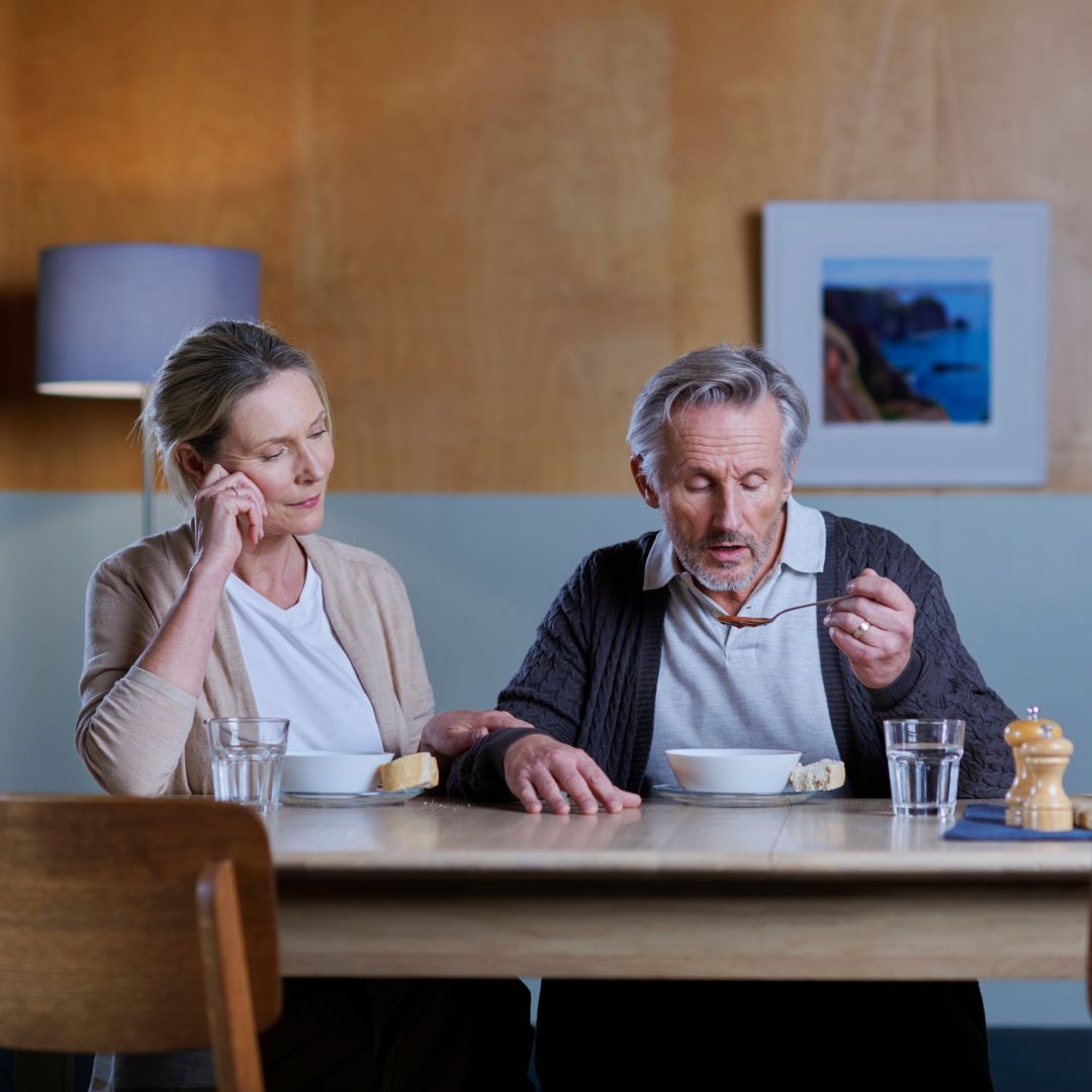 Twee personen zitten samen aan een tafel in een huiselijke omgeving met kommen en glazen op tafel.