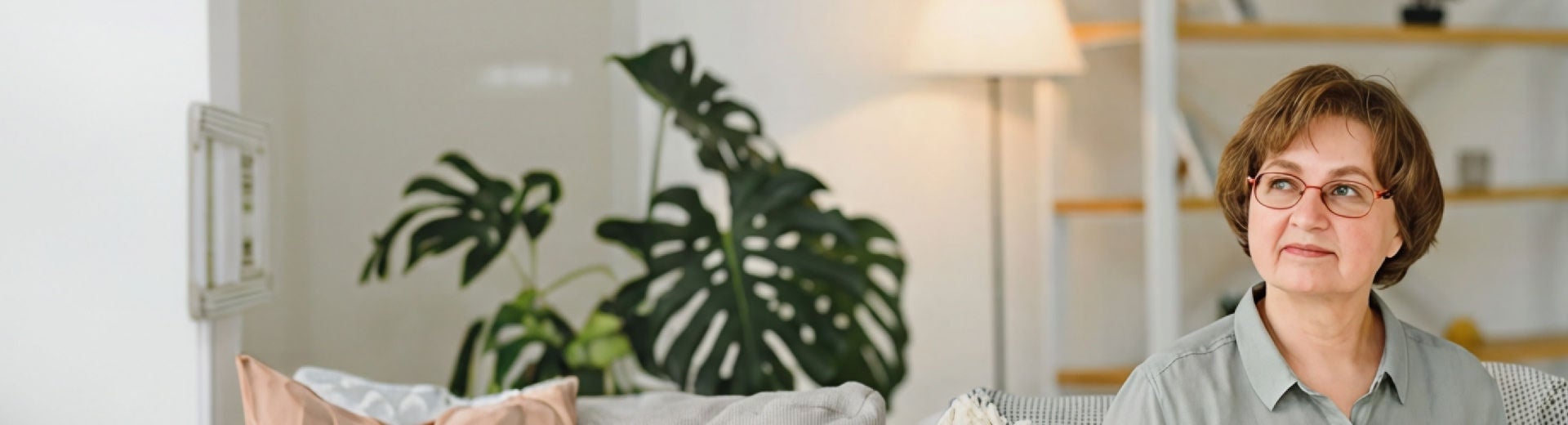 Una mujer está sentada en el sofá de su casa y sonríe con dulzura mientras sostiene una bebida Diben con sabor a albaricoque y durazno de Fresubin, que le ayuda a cubrir sus necesidades nutricionales y a controlar su diabetes. 