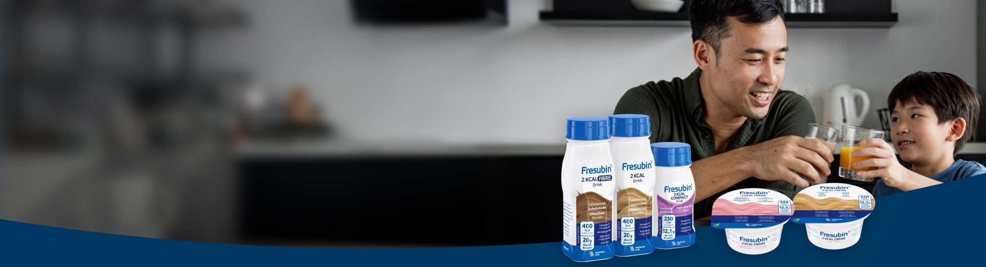 Un hombre sonriente está sentado junto a un niño pequeño en la encimera de la cocina, con la gama de productos Fresubin 2KCAL expuesta en primer plano, que incluye la bebida Fresubin 2KCAL FIBRE con sabor a chocolate, la bebida Fresubin 2KCAL con sabor a capuchino, la bebida Fresubin 2KCAL COMPACT con sabor a frutos del bosque y la bebida Fresubin 2KCAL Crème en sabores de fresa silvestre y praliné. 