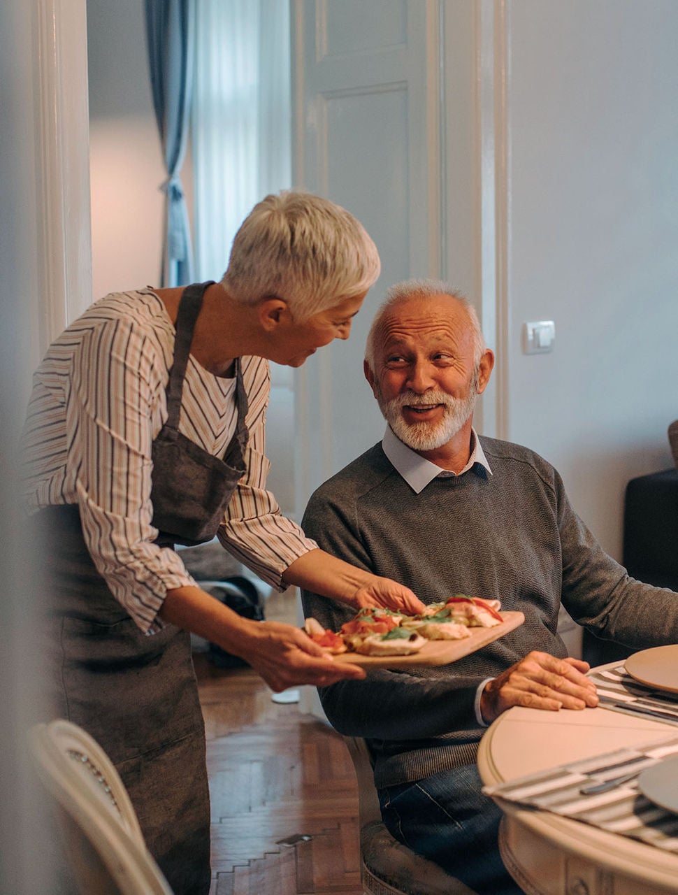 moteris prie stalo duoda išsirinkti maistą iš padėklo besišypsančiam vyrui