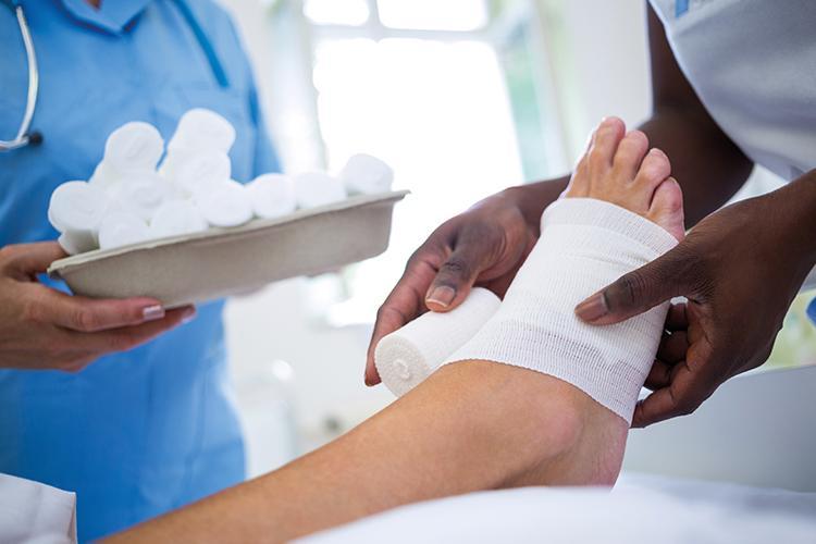 Ein Arzt legt einem Patienten einen Verband am Fuß an - verlinkt zu Wundheilungsstörung