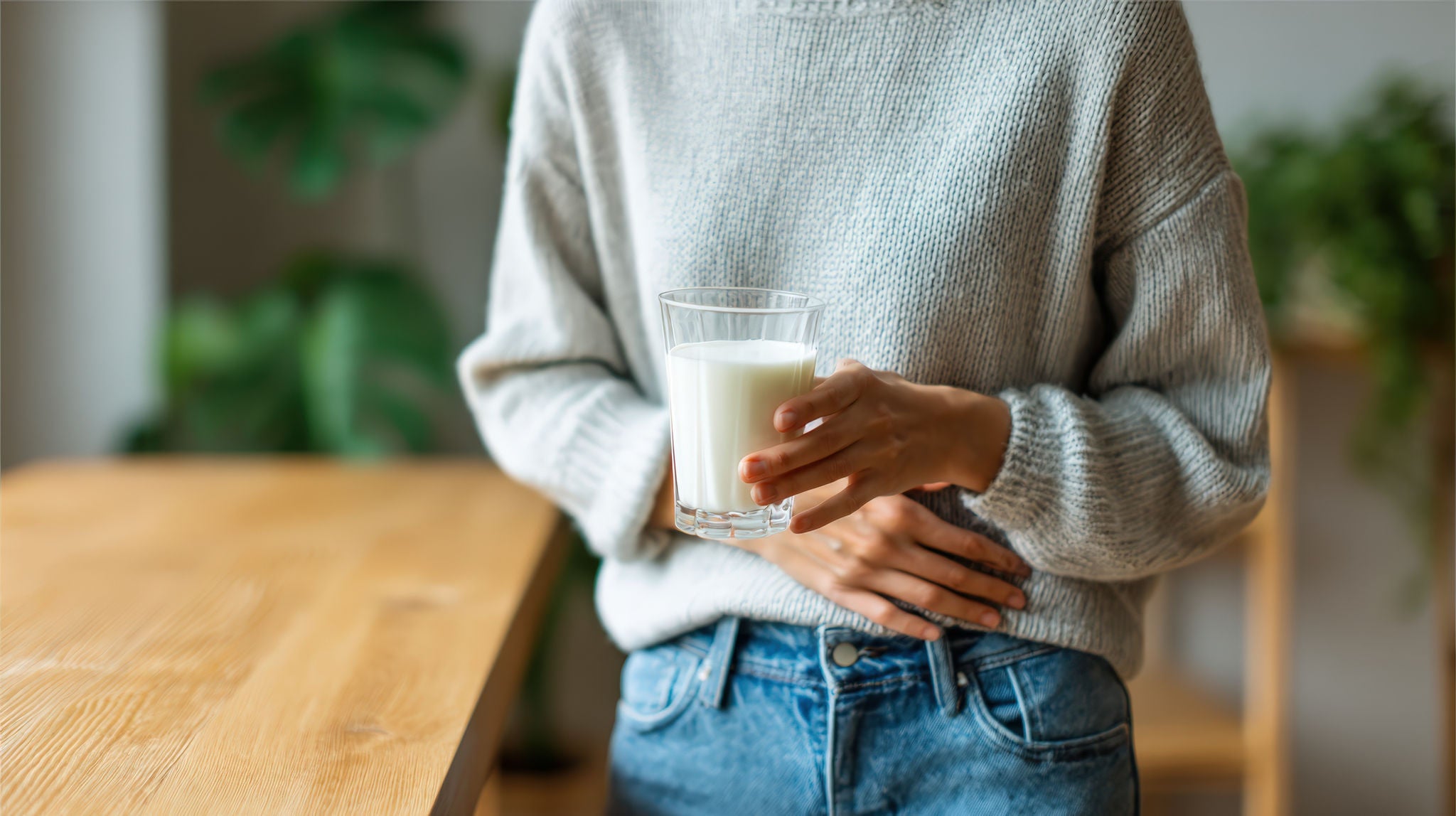 Woman holding glass of milk feeling abdominal discomfort, possibly due to lactose intolerance or digestive issue