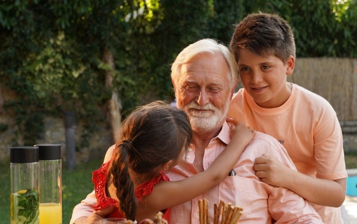 Un abuelo sonríe mientras disfruta del tiempo con sus nietos, sabiendo que sus necesidades nutricionales están cubiertas gracias a la gama de suplementos de Fresubin para personas mayores. 