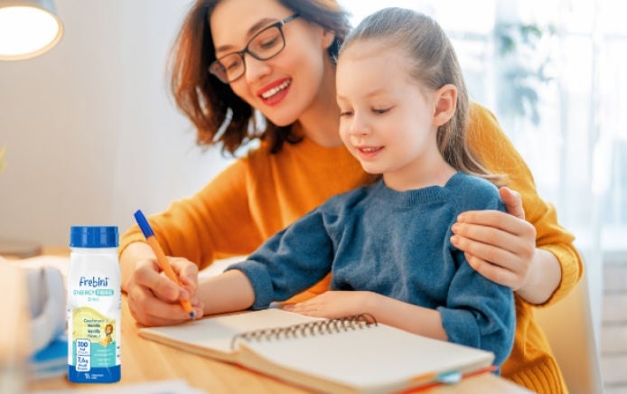 Una mamá y su hija sonríen mientras están sentadas dibujando juntas, sabiendo que la niña cuenta con el apoyo de la bebida ENERGY FIBRE de Fresubin con sabor a vainilla, un suplemento nutricional oral de la línea pediátrica de Frebini. 