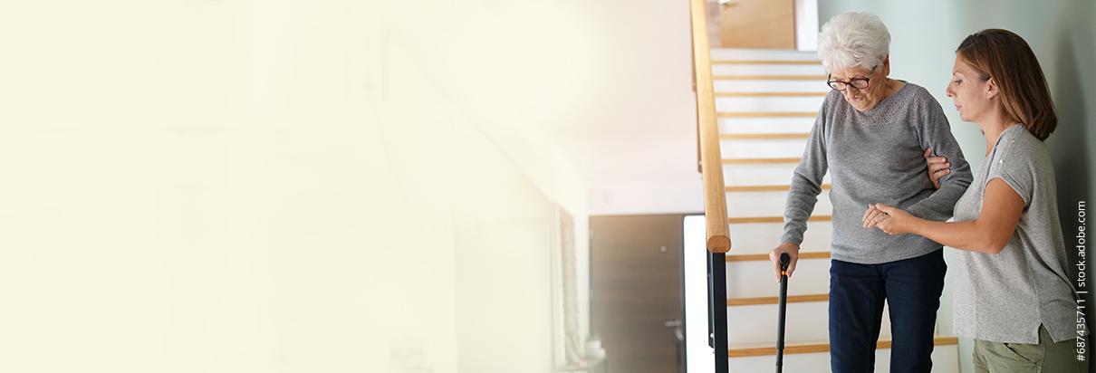 Ernährung bei Sarkopenie - Eine Pflegerin hilft einer Patientin mit Sarkopenie beim Herabsteigen einer Treppe.