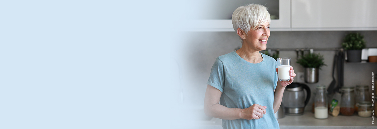 Lächelnde Frau genießt ein Glas laktosefreie Trinknahrung am Morgen.