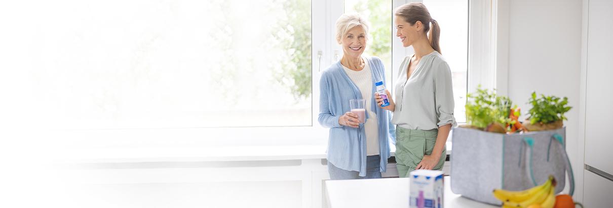 Patientin, die unter Mangelernährung leidet, nimmt Fresubin Trinknahrung im Glas zu sich. Ihre Tochter unterstützt sie bei der ausgewogenen Ernährung.
