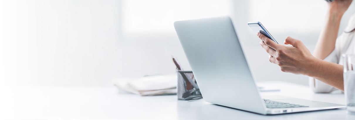 žmogus laiko išmanųjį telefoną prie kompiuterio