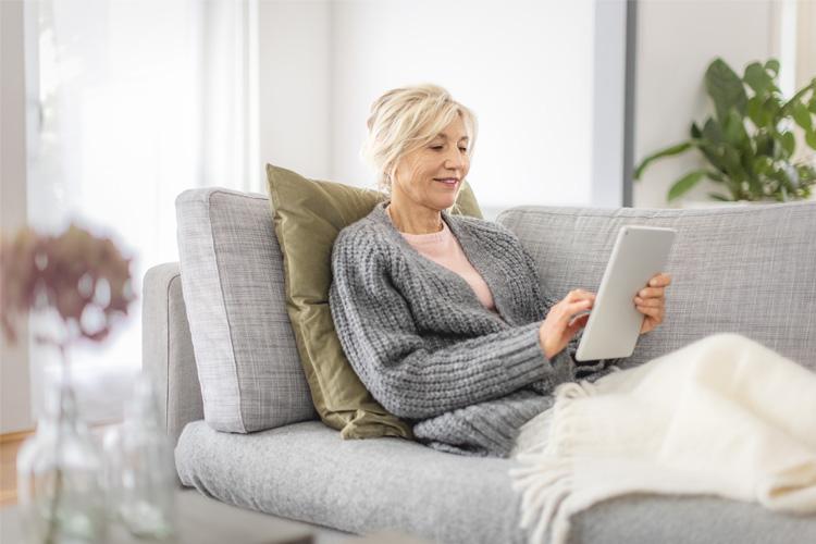 Patientin liegt auf dem Sofa und tippt auf ihrem Tablet, um einen Mangelernährungs-Test durchzuführen - verlinkt zu Mangelernährungs-Test.